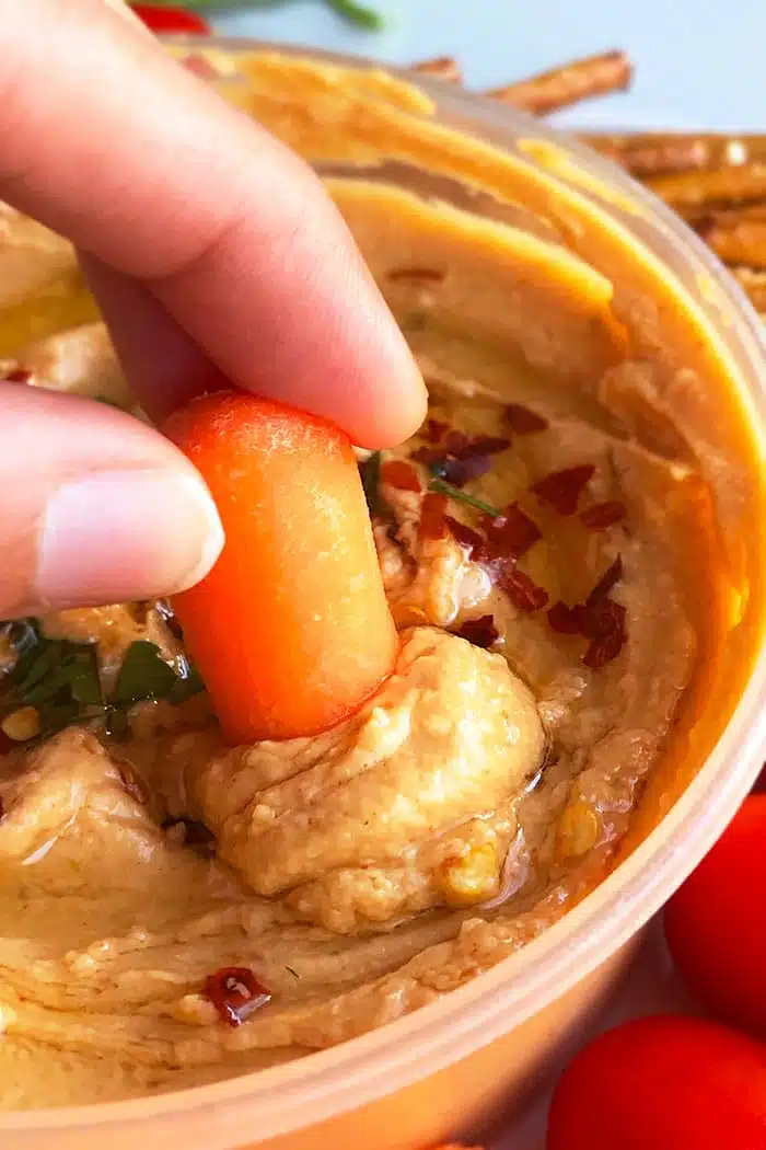 Baby Carrot Being Dipped in Roasted Red Pepper Hummus 