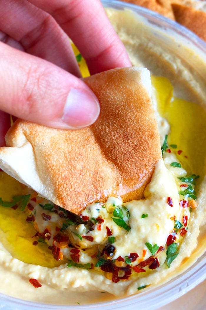 Pita Bread Being Dipped in Bowl of Hummus