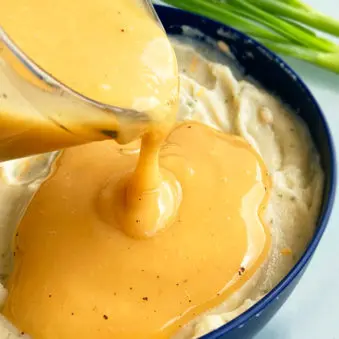 Homemade Chicken Gravy Being Poured Over Bowl of Mashed Potatoes