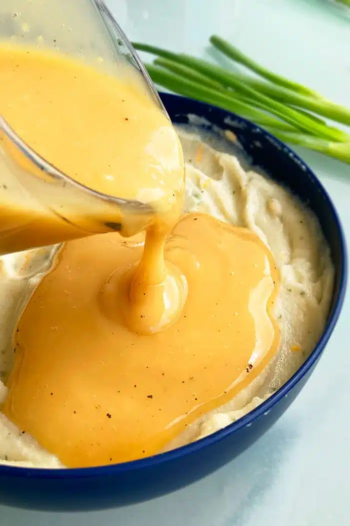 Homemade Chicken Gravy Being Poured Over Bowl of Mashed Potatoes