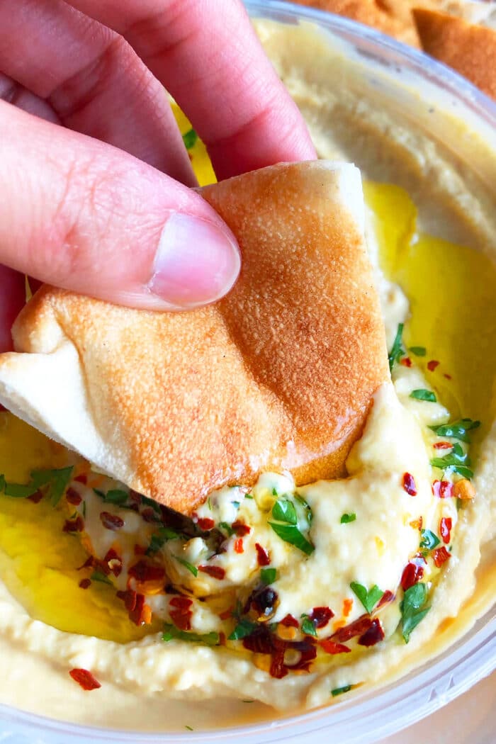 Pita Bread Being Dipped in Bowl of chickpea dip.