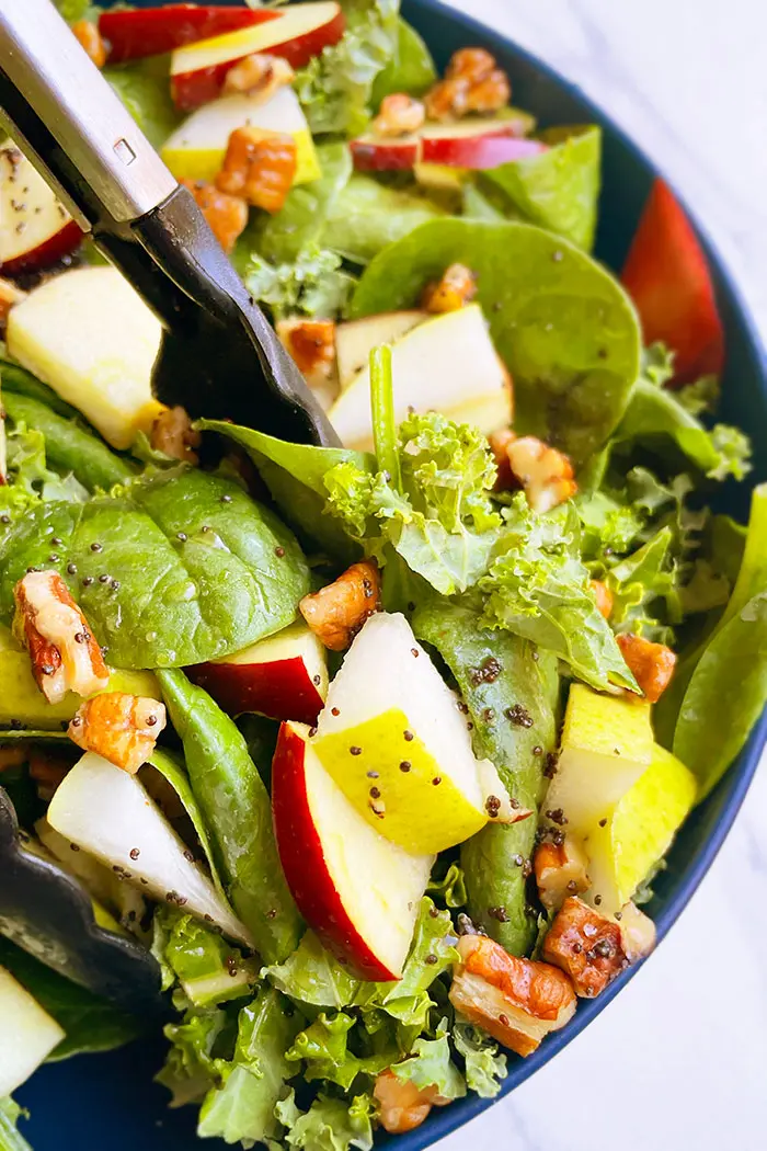 Tongs Holding the Best Thanksgiving Salad with Apples, Pears and Apple Cider Vinaigrette in Blue Bowl