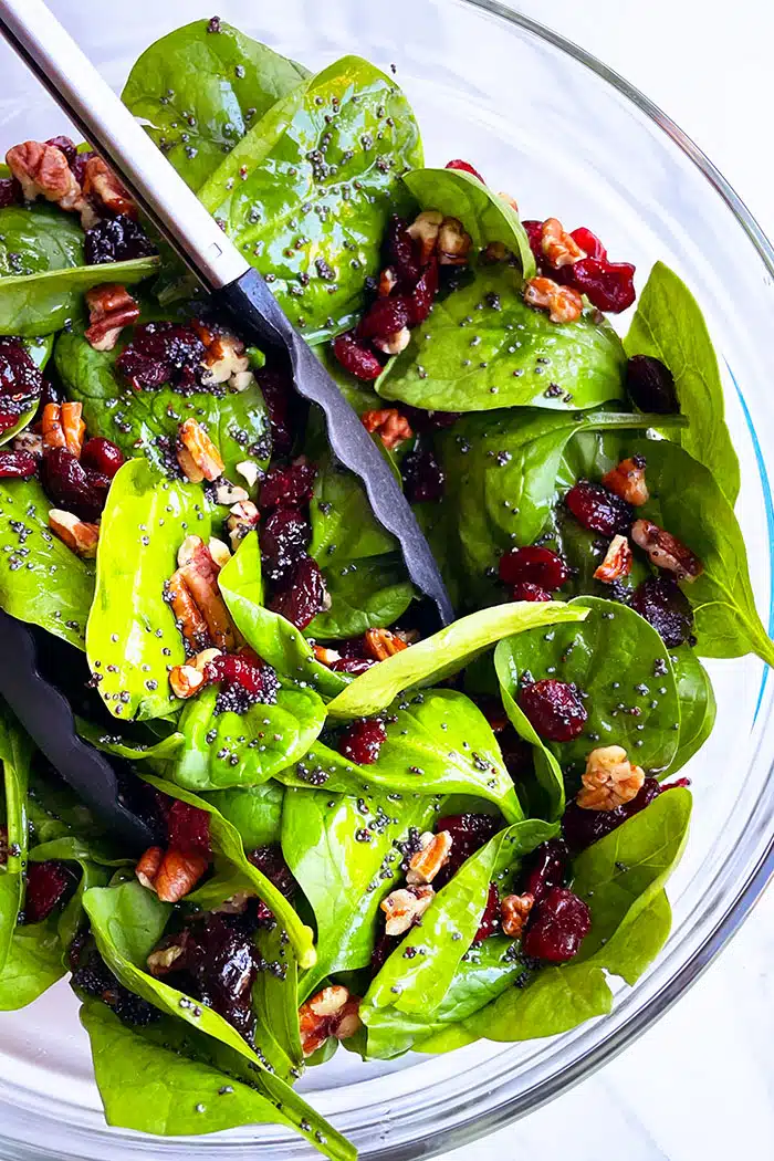 Tongs Full of Holiday Spinach Salad with Poppyseed Dressing on White Background