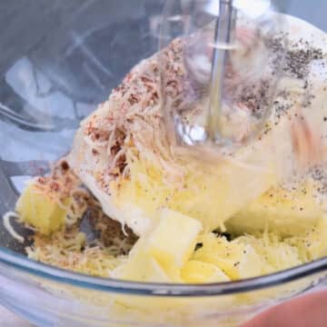 Cream cheese, butter, mozzarella cheese, salt, pepper, paprika, garlic powder in glass bowl being mixed with a hand held mixer. 