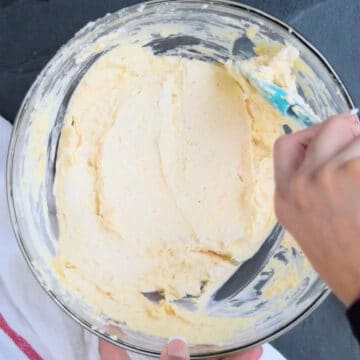 Cheese mixture being smoothed out with rubber spatula. 