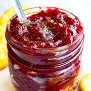 Best Easy Homemade One Pot Apple Cranberry Chutney In Glass Jar on White Marble Background.