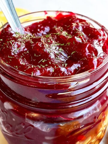 Best Easy Homemade One Pot Apple Cranberry Chutney In Glass Jar on White Marble Background.