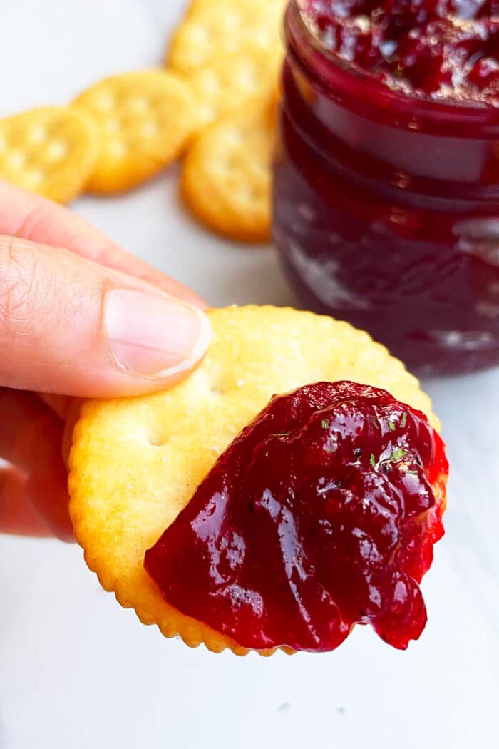 Fingers Holding Ritz Cracker That's Spread with Christmas Chutney.