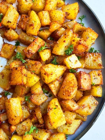 Easy Crispy Oven Baked Breakfast Potatoes in Navy Blue Plate on White Background