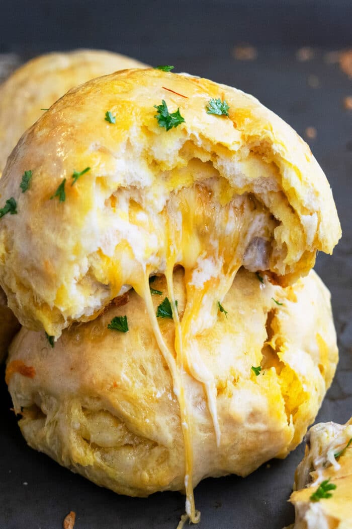 Stack of Two Stuffed Garlic Cheese Bombs on Black Baking Tray With Cheese Melting Out.