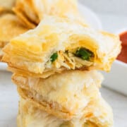 Stack of Chicken Puff Pastry (Also Called Chicken Parcels or Chicken Patties) on White Background With One Partially Eaten.