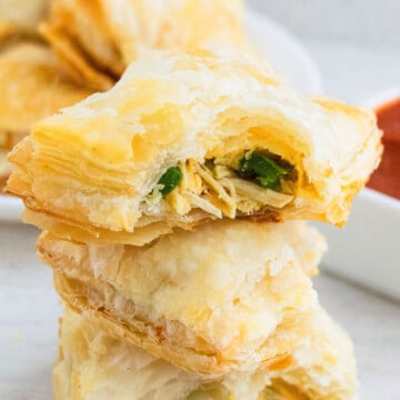 Stack of Chicken Puff Pastry (Also Called Chicken Parcels or Chicken Patties) on White Background With One Partially Eaten.