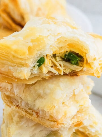 Stack of Chicken Puff Pastry (Also Called Chicken Parcels or Chicken Patties) on White Background With One Partially Eaten.