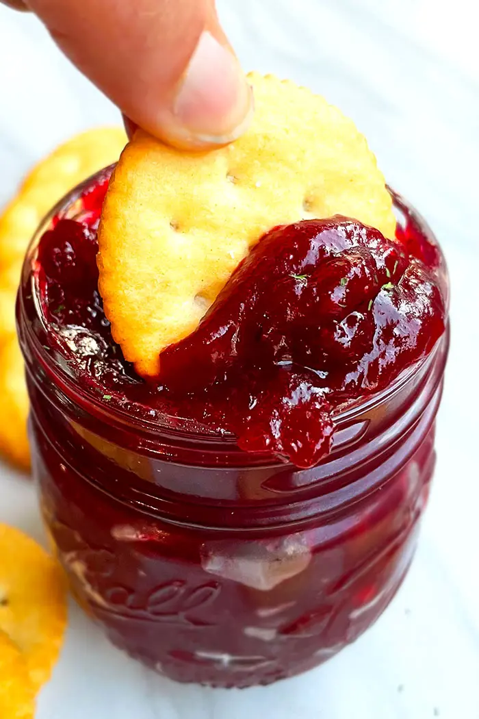 Sweet and Spicy Cranberry Apple Chutney in Glass Jar With Ritz Cracker on White Background