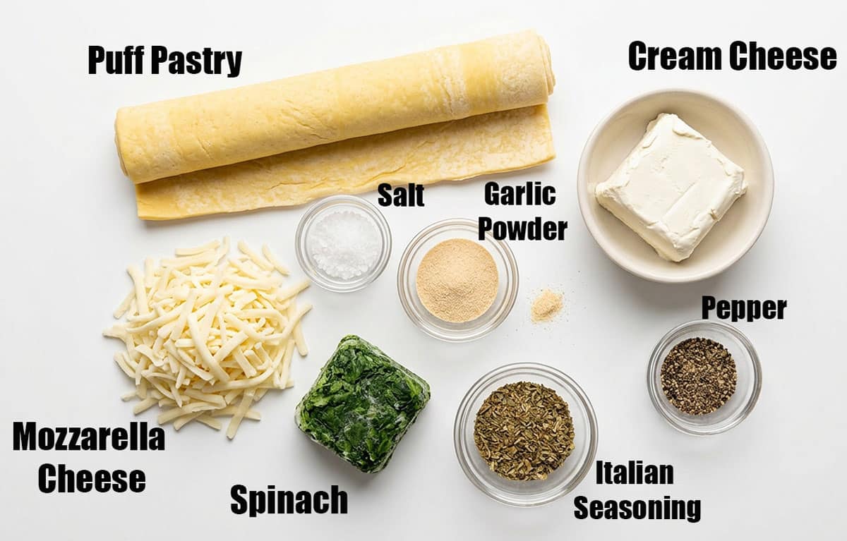 Ingredients for recipe on white background- pastry dough, cheese, spices, spinach. 