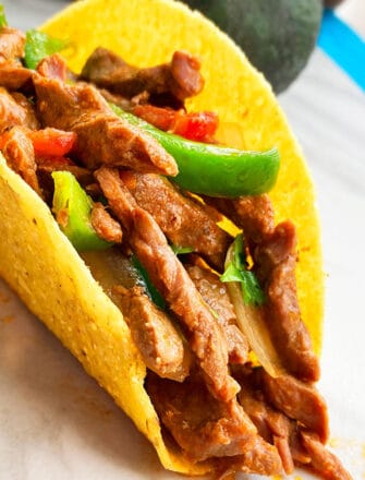 Instant Pot Flank Steak Tacos in Hard Tortilla Shell on White Background