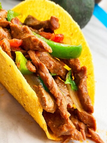 Instant Pot Flank Steak Tacos in Hard Tortilla Shell on White Background