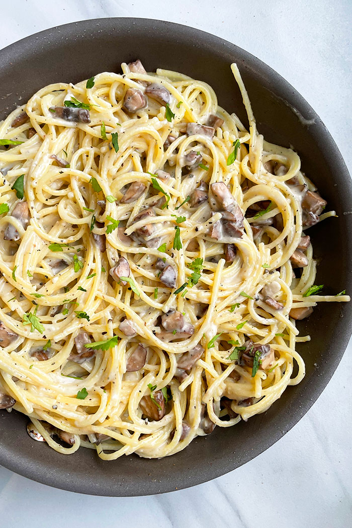 Overhead Shot of Spaghetti with Mushrooms and White Parmesan Cheese Sauce in Black Nonstick Pot