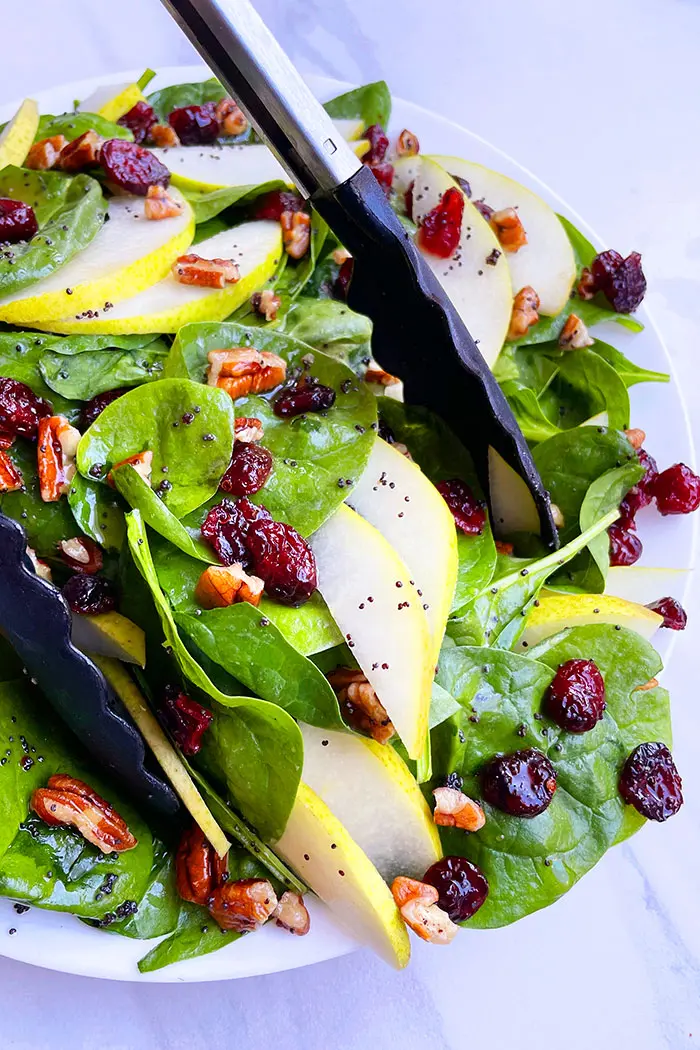 Tongs Full of Best Pear Salad in White Plate with Bluish White Background