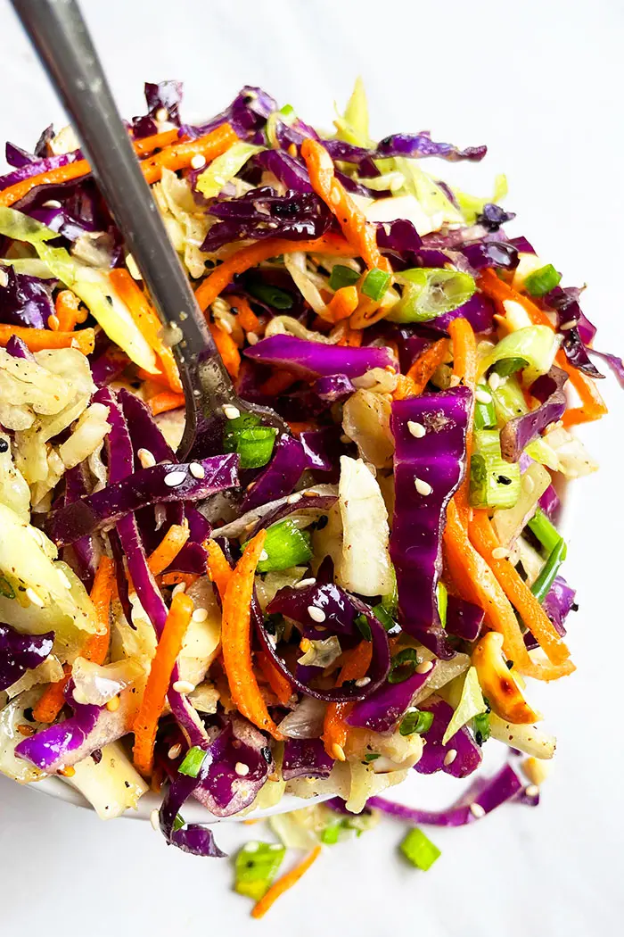 Asian Coleslaw in White Bowl With a Silver Fork on White Background- Overhead Shot