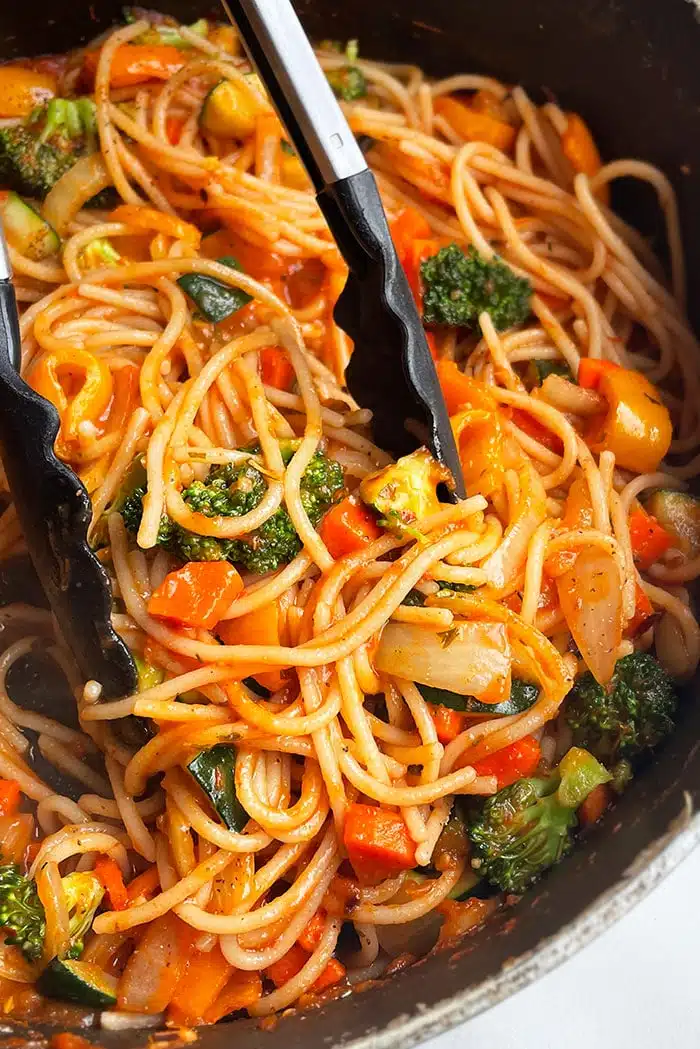 Tongs Holding Easy Vegetable Pasta in Black Pot 