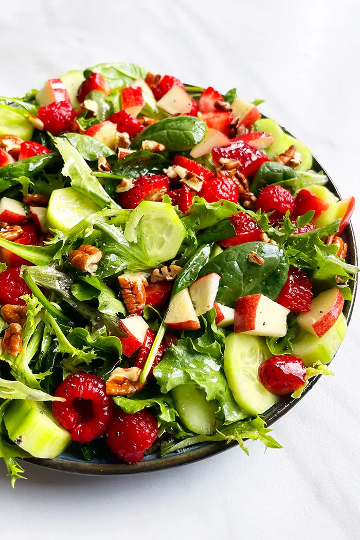 Homemade Salad With Orange Vinaigrette in Black Plate on White Background