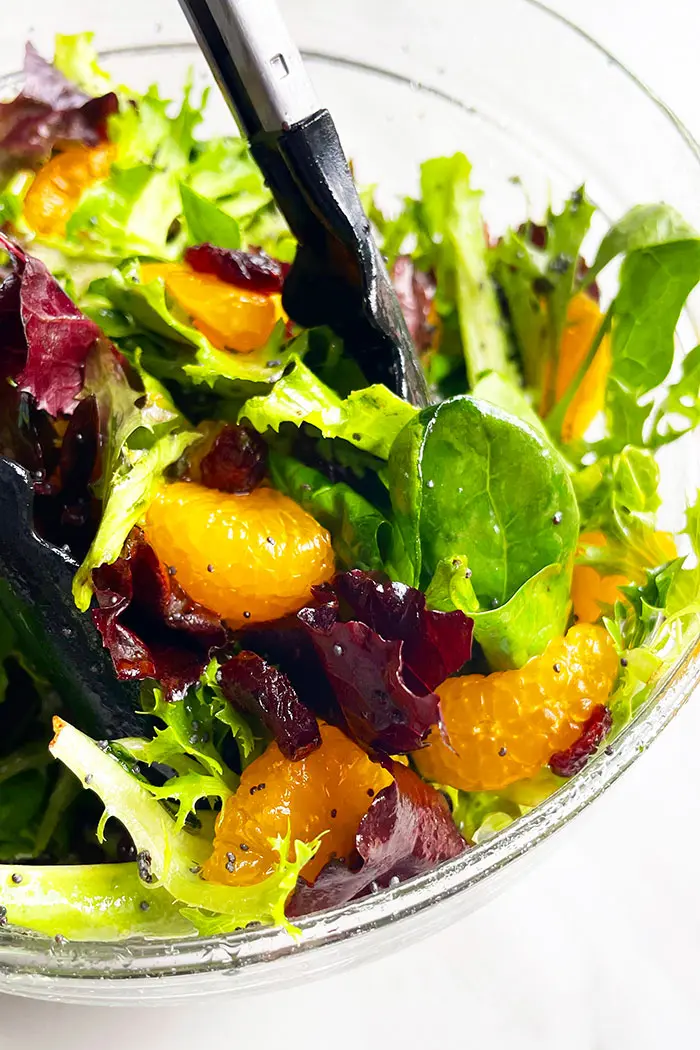 Tongs Full of Classic Arugula Spinach Orange Salad With Orange Dressing and Cranberries in Glass Bowl