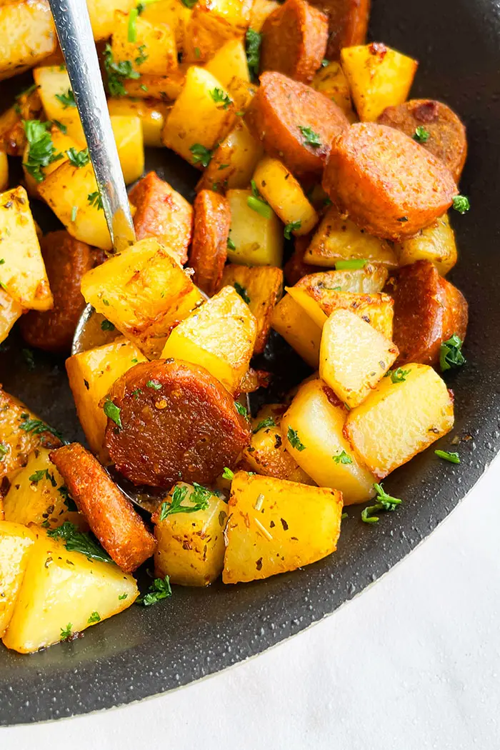 Crispy Potatoes With Sausages in a Spoon- Angled Shot