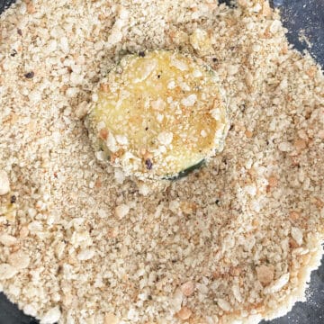 Egg coated zucchini being coated in breadcrumbs.