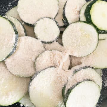 Zucchini cut into circles that is being coated in flour.