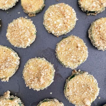 Coated zucchini rounds placed on an unlined baking tray.