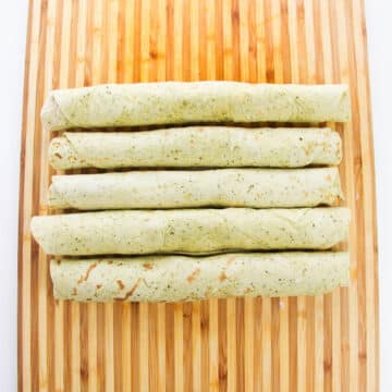 Logs of filled tortillas on a cutting board. 