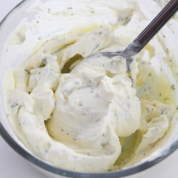 Cream cheese and ranch seasoning being mixed together with a spoon in a glass bowl. 