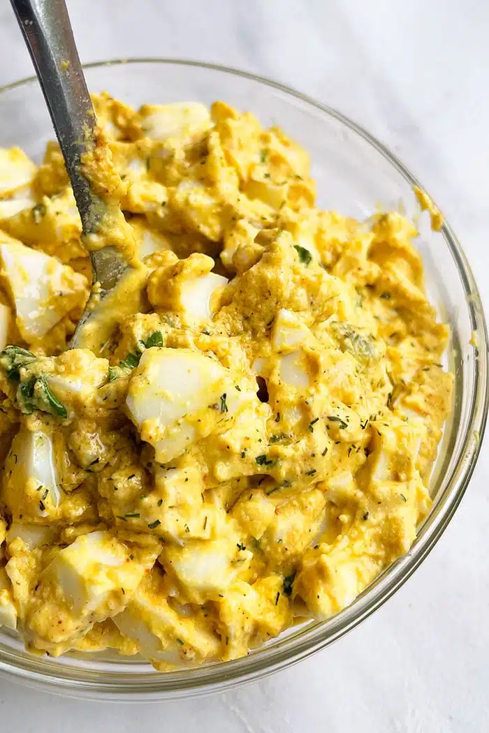 Spoonful of Easy Egg Salad in Glass Bowl on Marble Background 