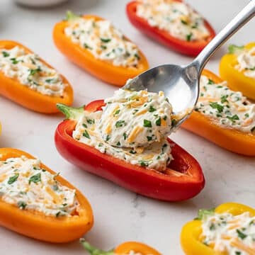 Cheese mixture being stuffed into peppers with a spoon.