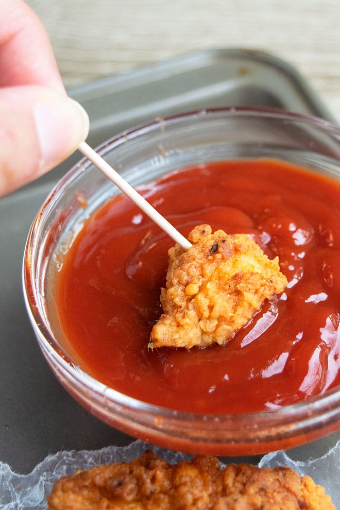 Breaded Chicken Bites on Toothpick Being Dipped in Bowl of Ketchup