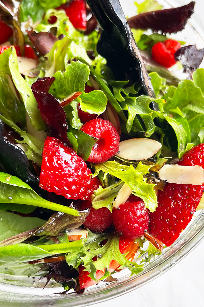 Tongs Full of Salad With Strawberries, Raspberries, Almonds in Glass Bowl- Closeup Shot