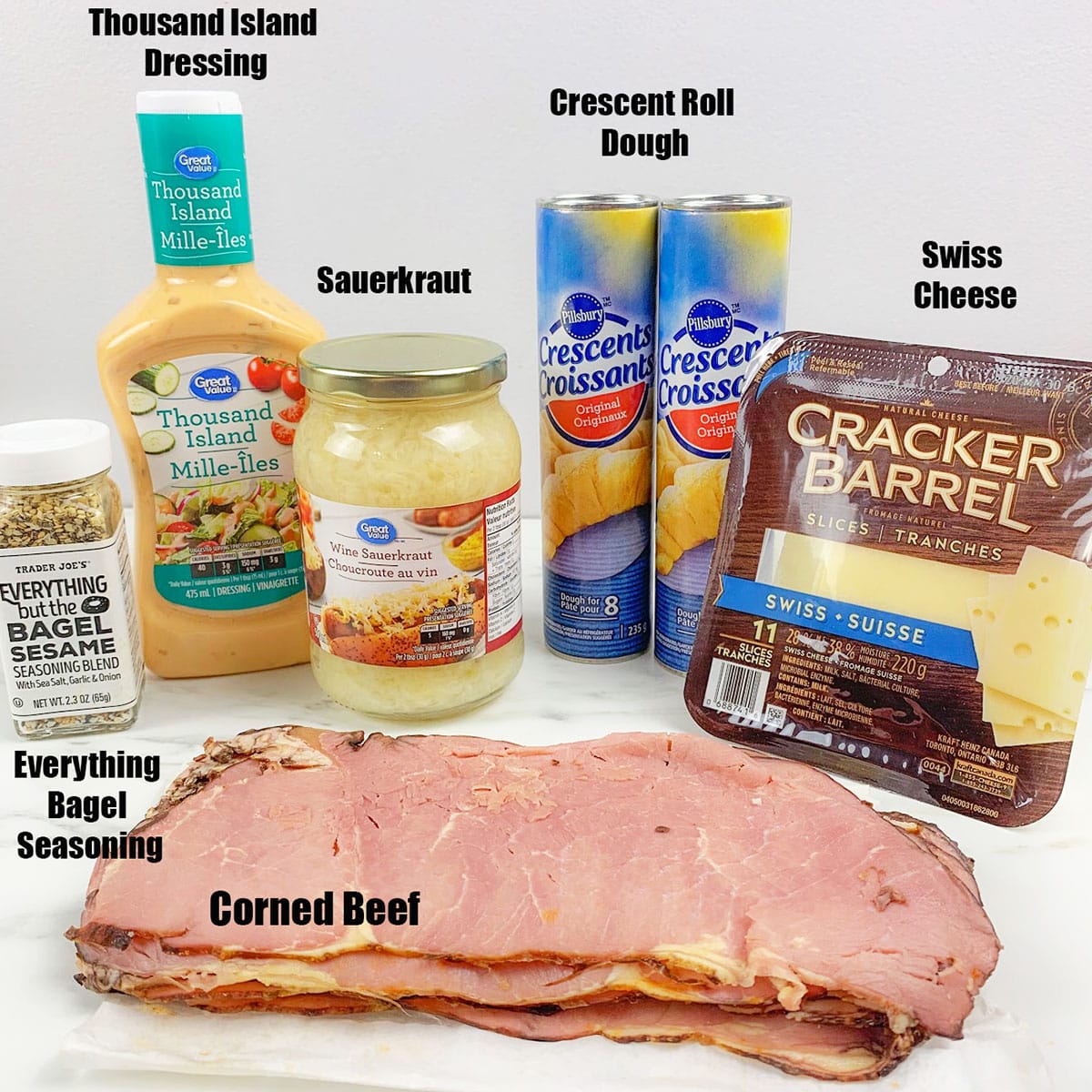 Ingredients for recipe on white background- seasoning, corned beef, crescent dough, cheese, sauerkraut, dressing.