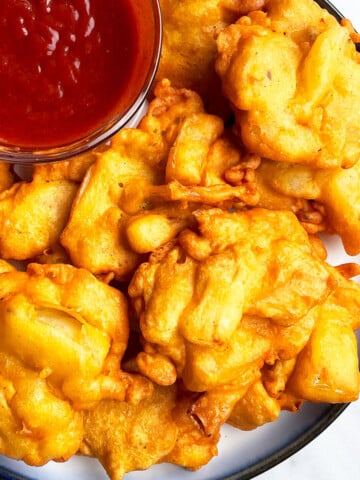 Easy One Pot Crispy Onion Fritters (Indian Pakoda) in White Dish With Bowl of Red Dipping Sauce.