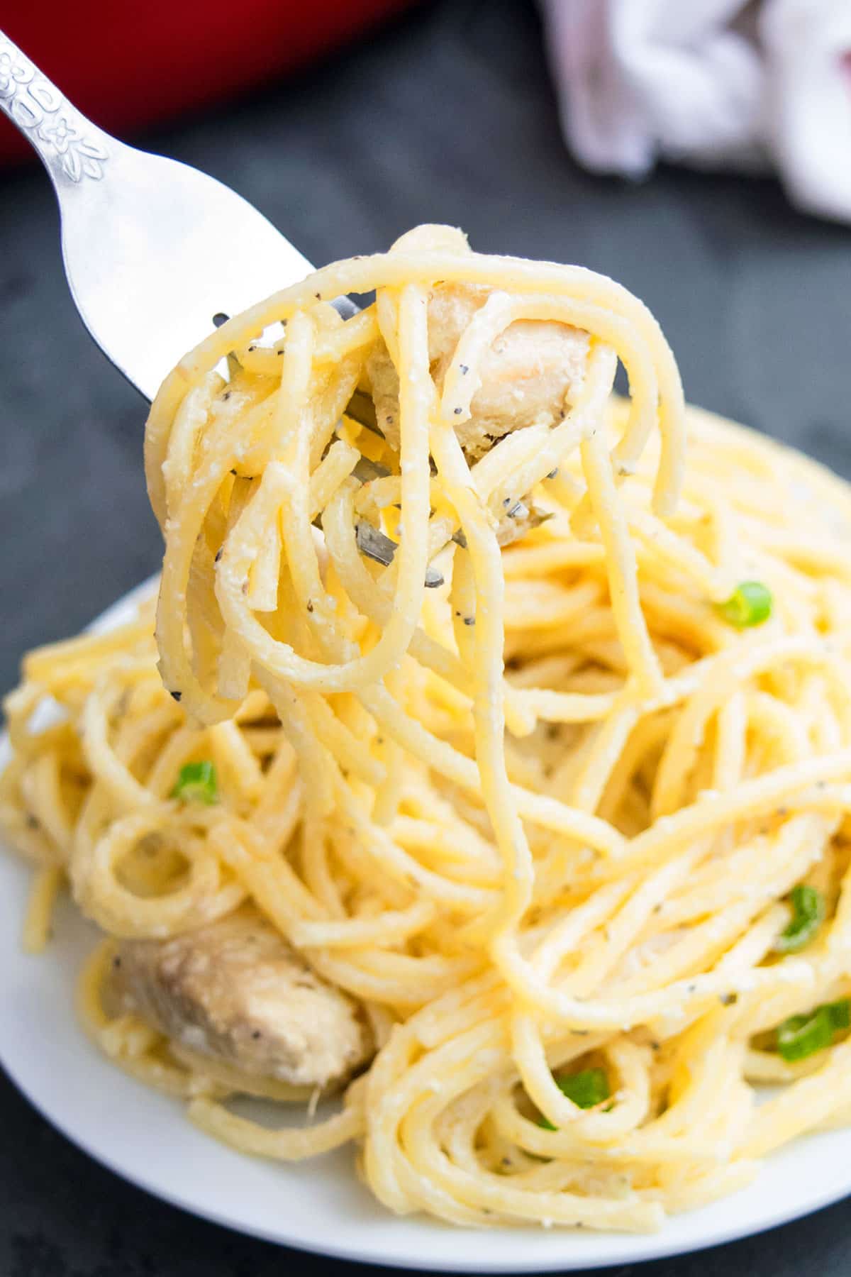 Fork Full of Butter Pasta With Chicken Over a White Dish. 