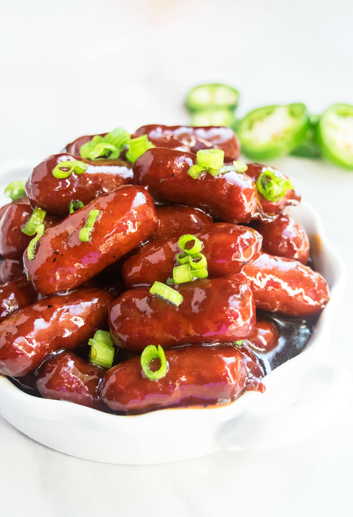 White dish filled with grape jelly little smokies and topped off with green onion garnish.