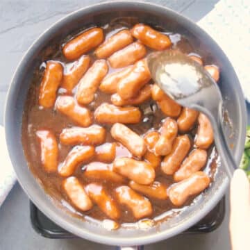 Mini sausages added to sauce and being mixed with a big black spoon. 