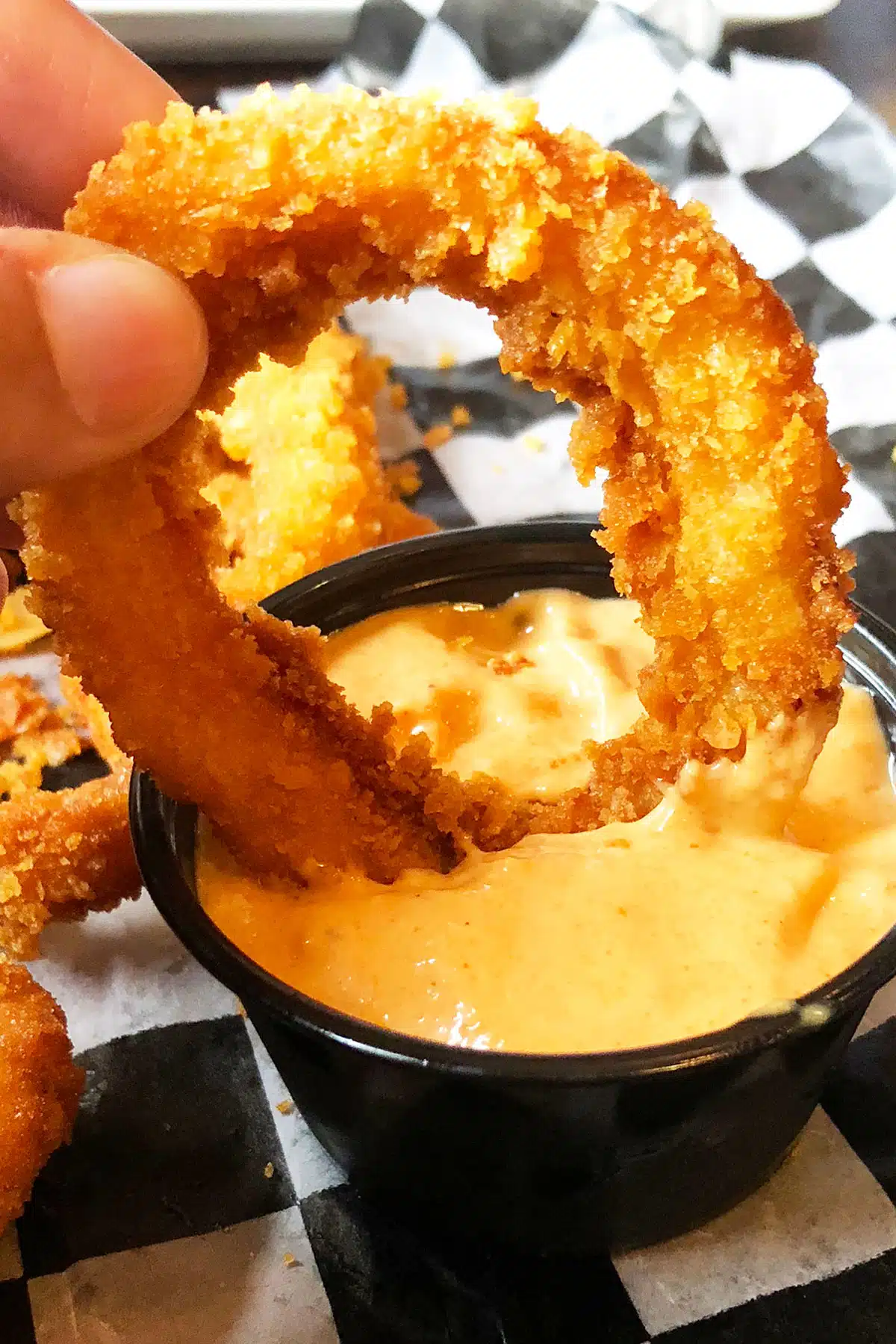 Closeup Shot Breaded Onion Being Dipped in a Small Bowl of Sriracha Mayo Sauce. 