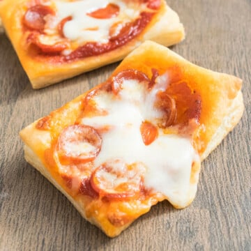 Easy mini puff pastry pizza with mini pepperoni and melted cheese on wood background.