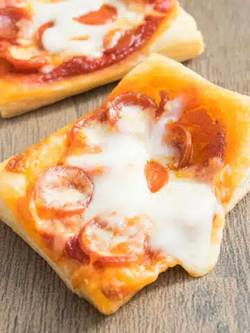 Easy mini puff pastry pizza with mini pepperoni and melted cheese on wood background.