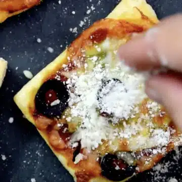 Parmesan cheese being sprinkled on top of mini appetizer. 