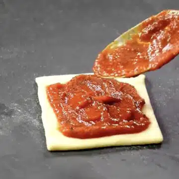Pizza sauce being spread on top of dough. 