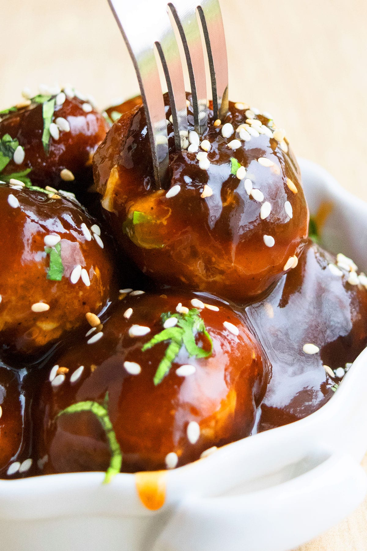 Fork being pushed into white dish of sweet and spicy Korean meatballs. 