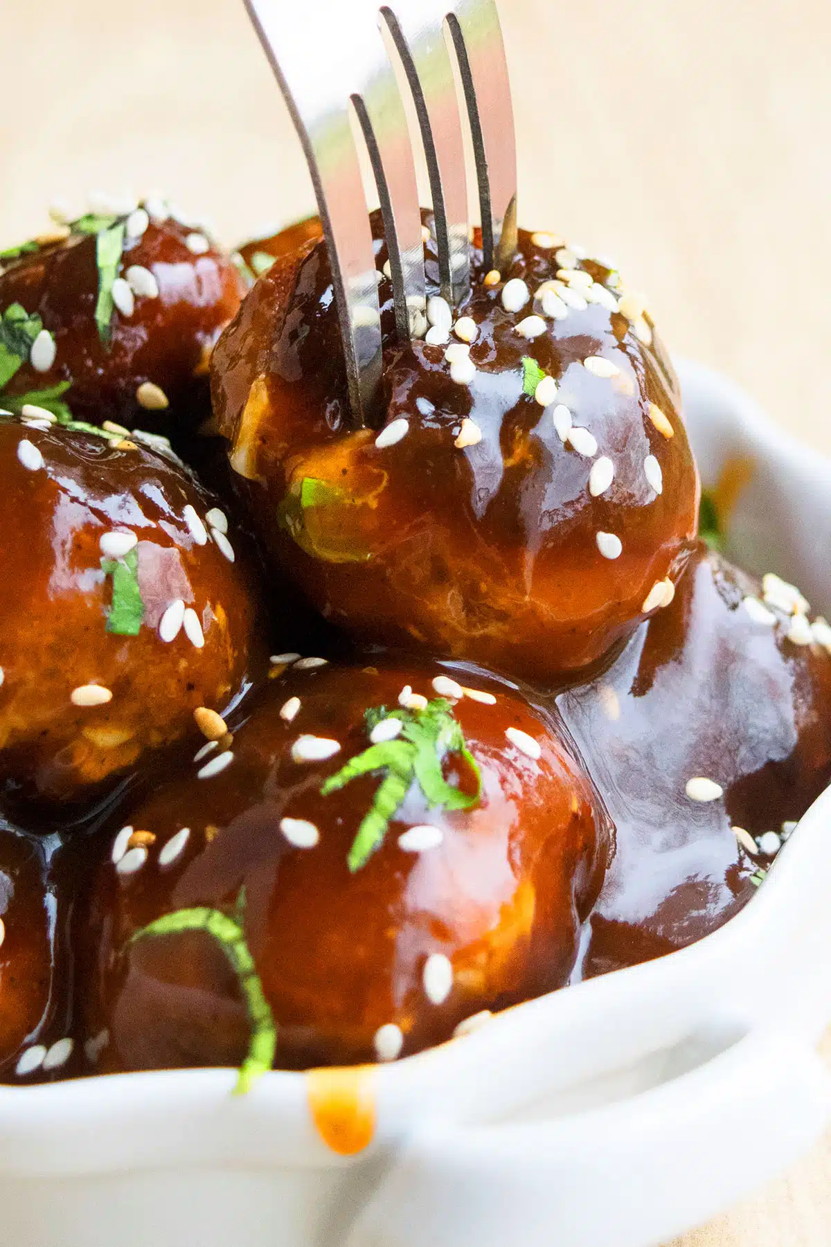 Fork being pushed into white dish of sweet and spicy Korean meatballs. 