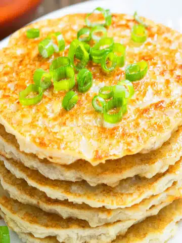 Stack of easy crispy leftover mashed potato pancakes with green onion garnish on white dish.